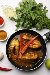 Photo of Tasty fish curry in frying pan and ingredients on white tiled table, flat lay. Indian cuisine