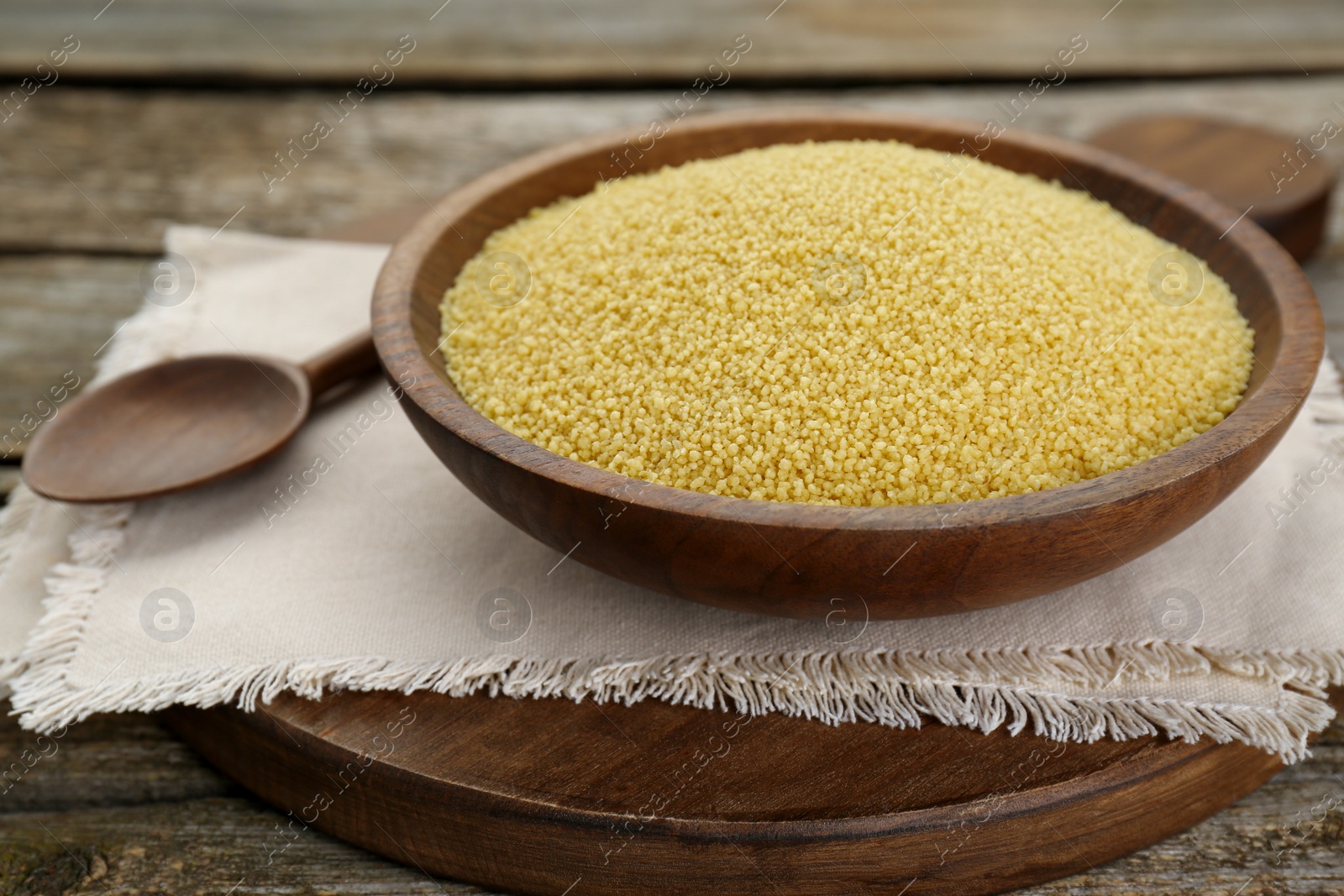 Photo of Bowl of raw couscous on wooden table, closeup