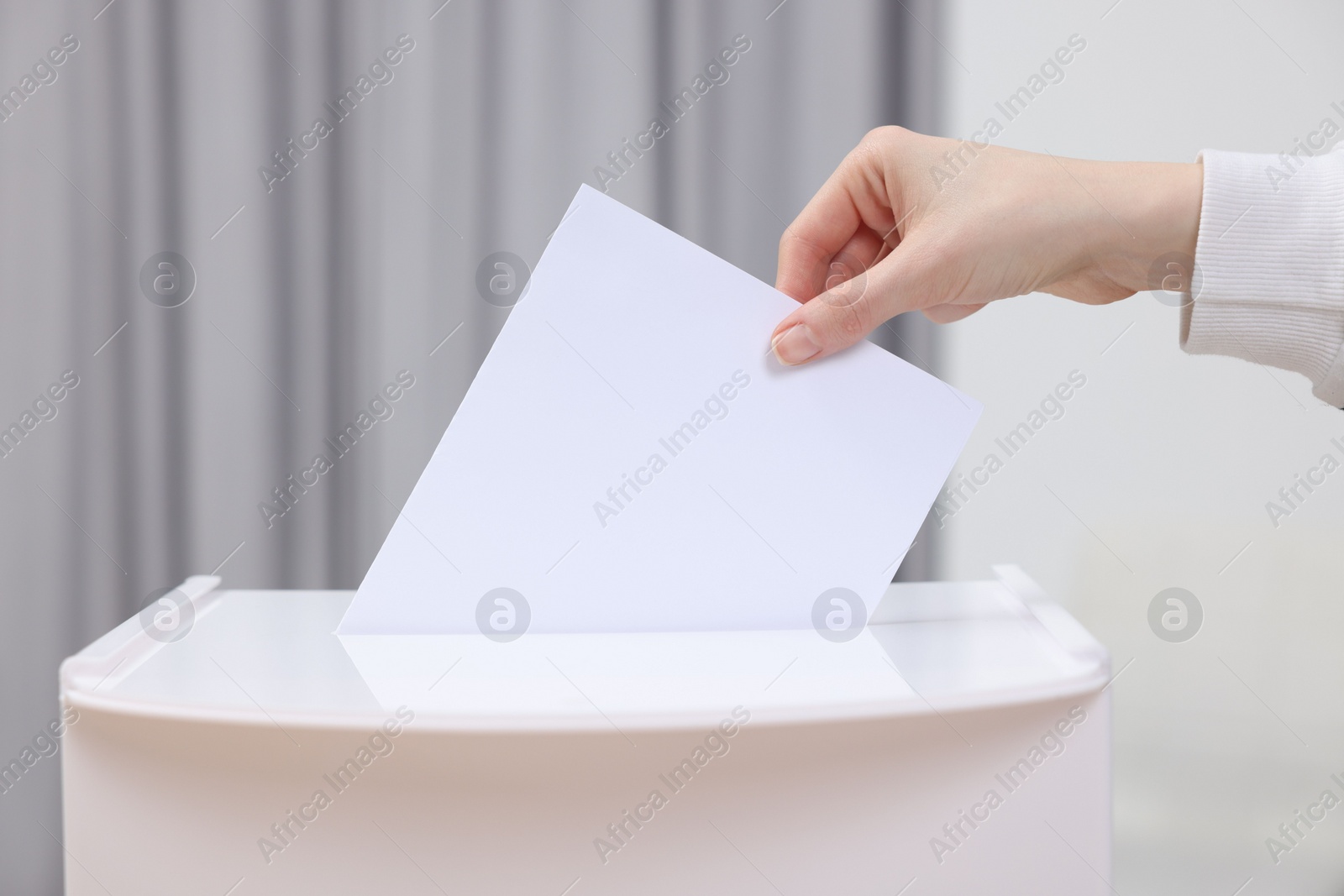 Photo of Woman putting her vote into ballot box on blurred background, closeup