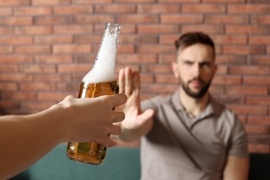 Man refusing to drink beer indoors, closeup. Alcohol addiction treatment