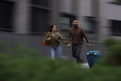 Being late. Young couple with suitcase running on city street. Motion blur effect