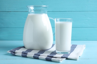 Photo of Jug and glass with fresh milk on light blue wooden table