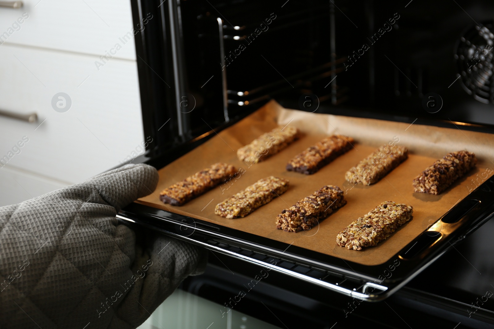 Photo of Woman taking delicious healthy granola bars from oven, closeup