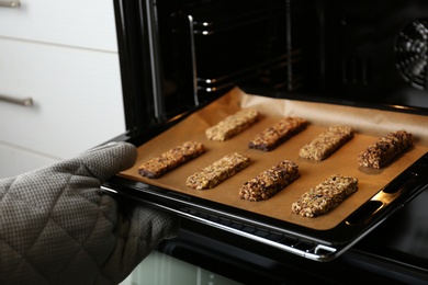 Woman taking delicious healthy granola bars from oven, closeup