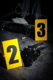 Photo of Shell casing, gun and crime scene markers on grey stone table