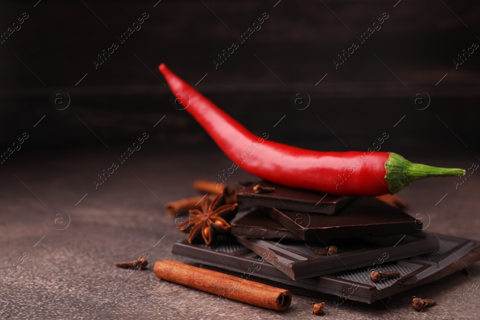 Photo of Delicious chocolate, fresh chili pepper and spices on grey textured table, closeup. Space for text