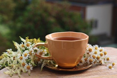 Cup of delicious chamomile tea and fresh flowers outdoors