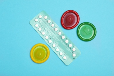 Condoms and birth control pills on light blue background, flat lay. Safe sex concept