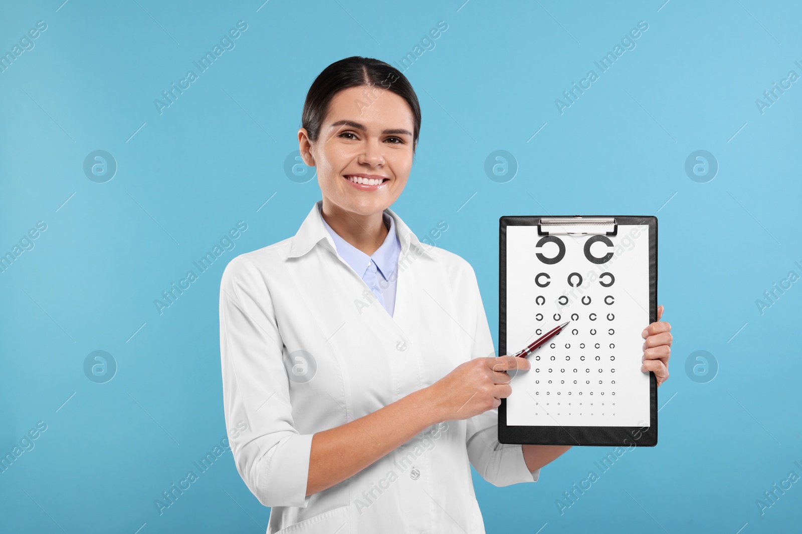 Photo of Ophthalmologist pointing at vision test chart on light blue background