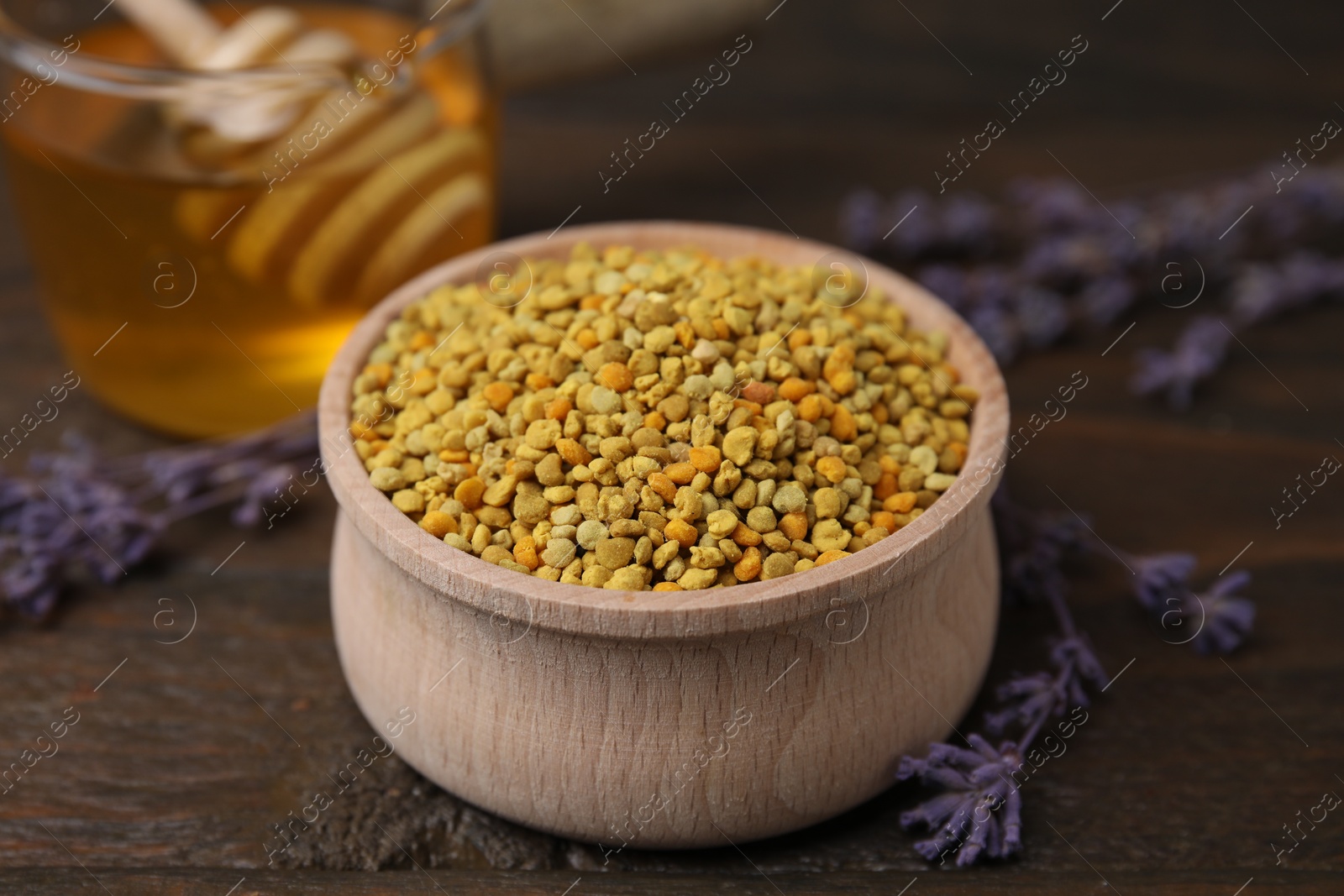 Photo of Fresh bee pollen granules in bowl, lavender and honey on wooden table, closeup