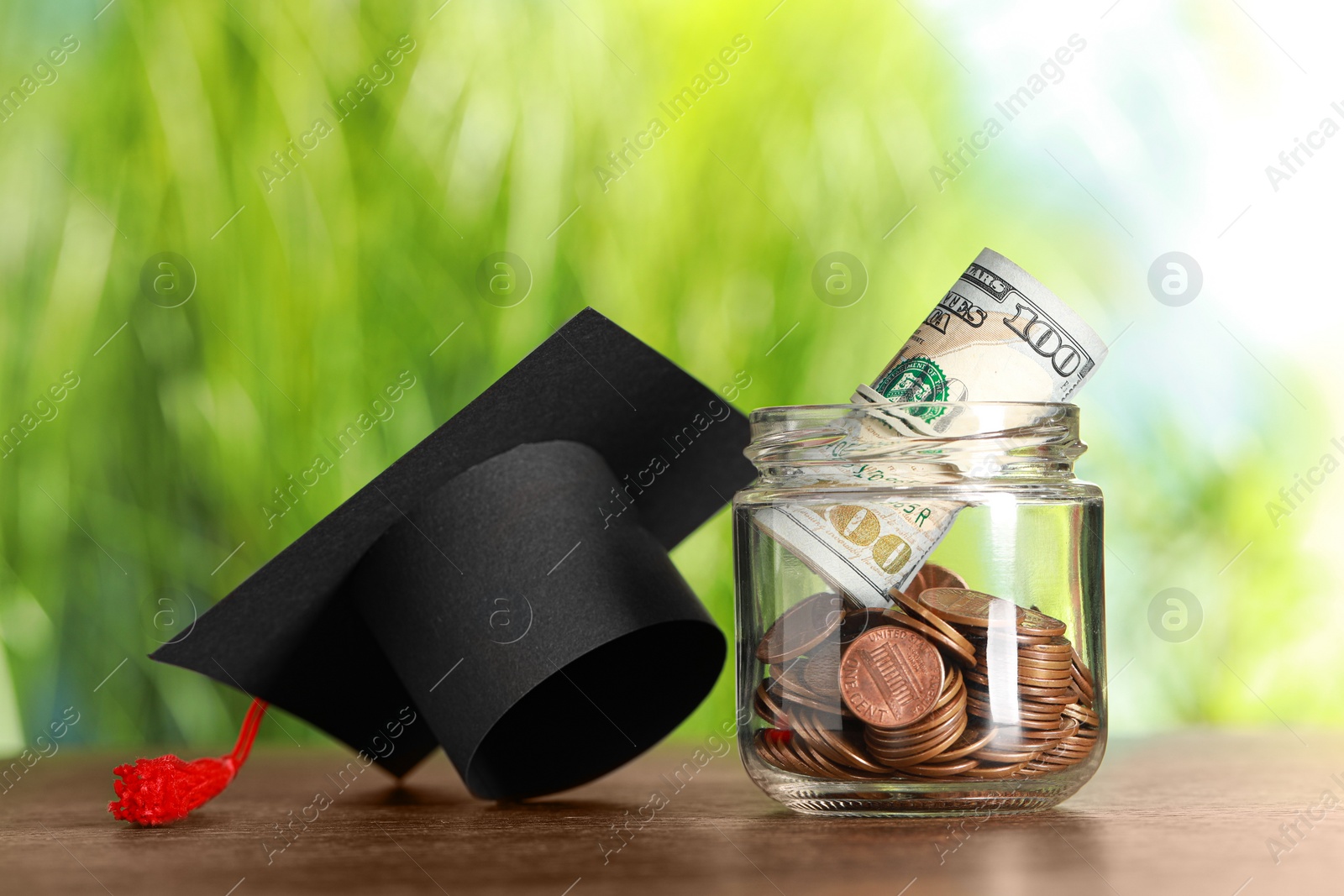 Photo of Scholarship concept. Glass jar with coins, dollar banknotes and graduation cap on wooden table