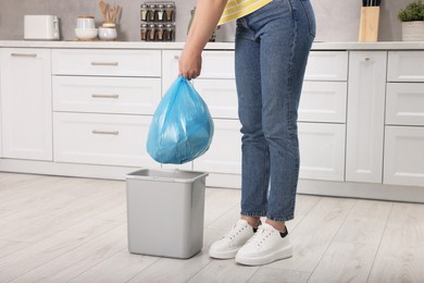 Photo of Woman taking garbage bag out of trash bin in kitchen, closeup