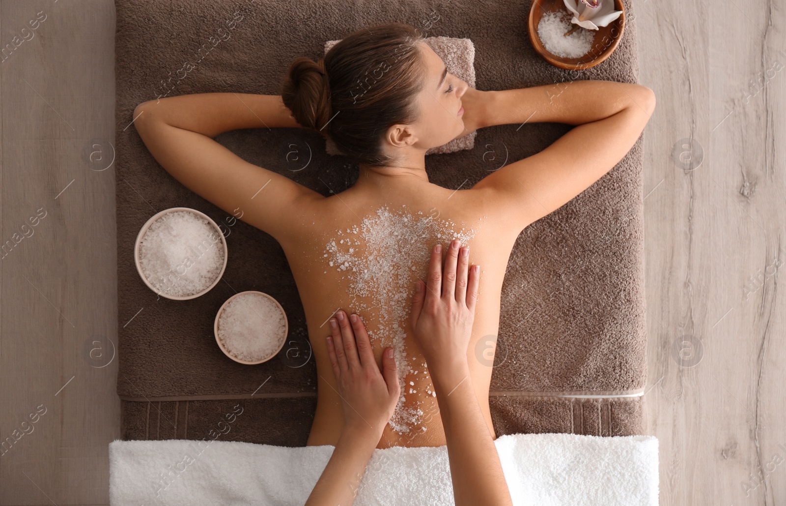 Photo of Young woman having body scrubbing procedure with sea salt in spa salon, top view