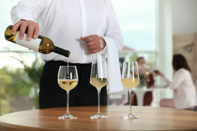 Waiter pouring wine into glass in restaurant, closeup