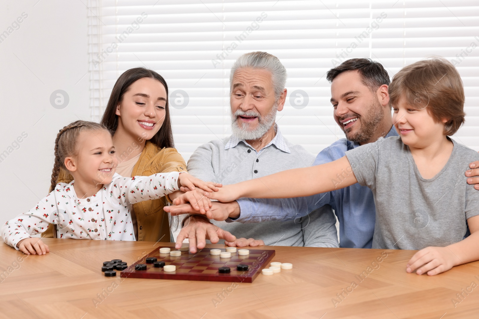 Photo of Happy family playing checkers at table in room