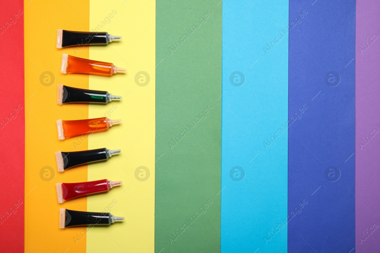 Photo of Tubes with different food coloring on rainbow background, flat lay. Space for text