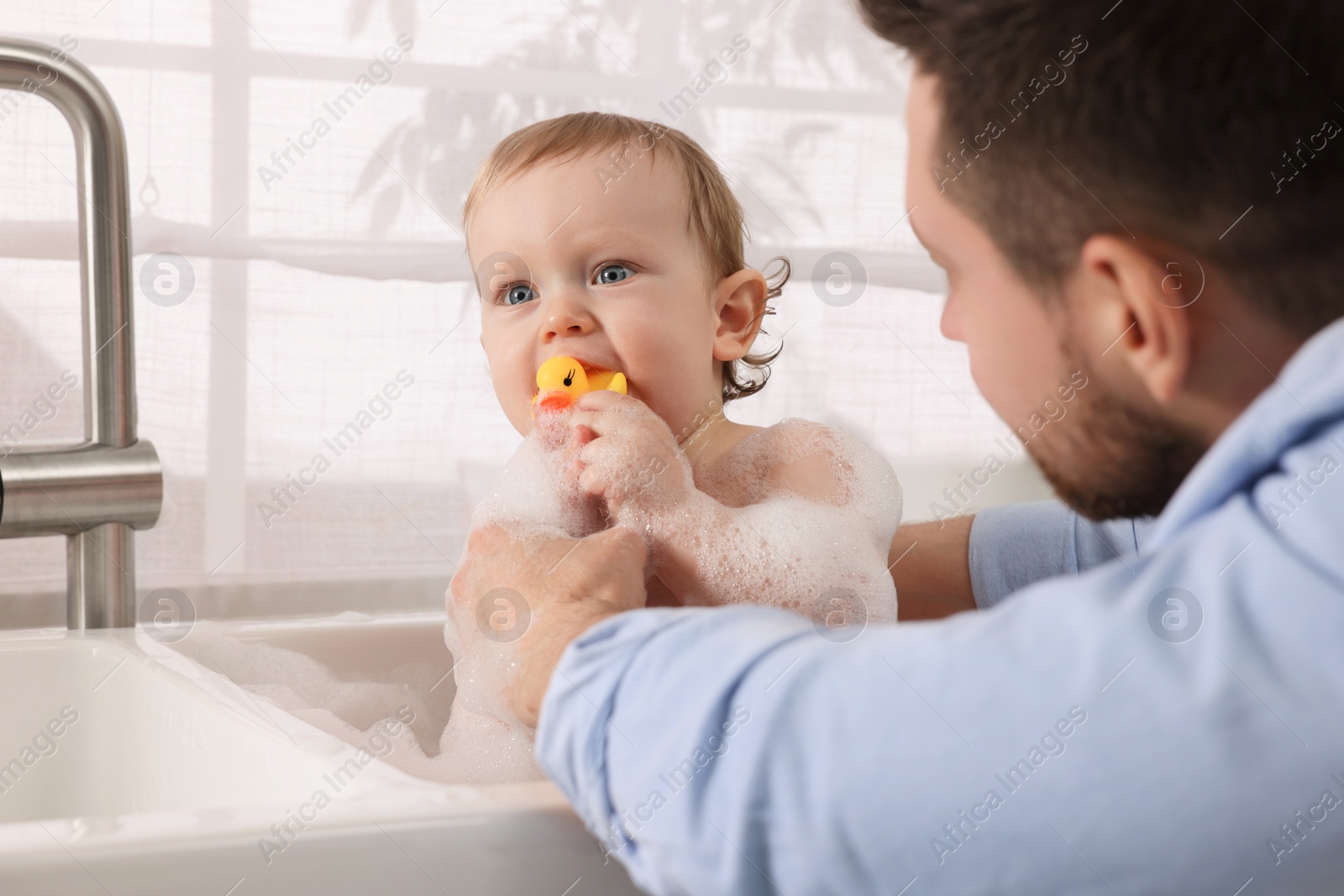 Photo of Father washing his little baby in sink indoors