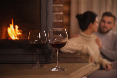 Photo of Lovely couple resting near fireplace, focus on glasses with red wine