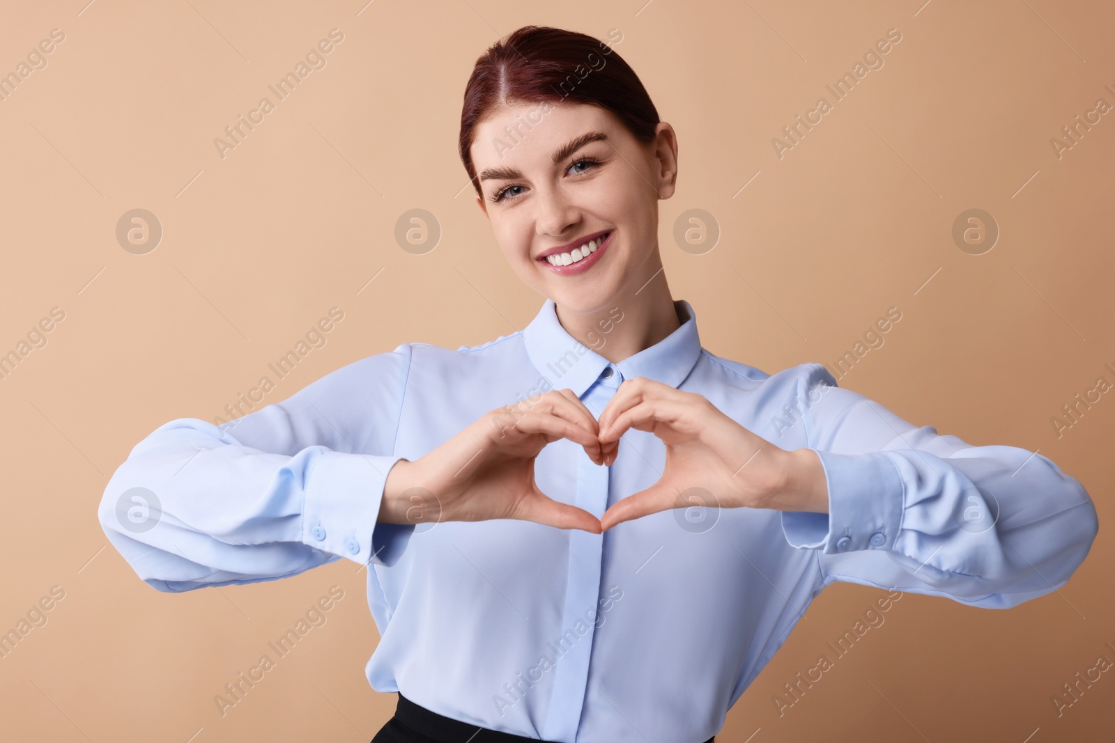 Photo of Happy young woman showing heart gesture with hands on beige background