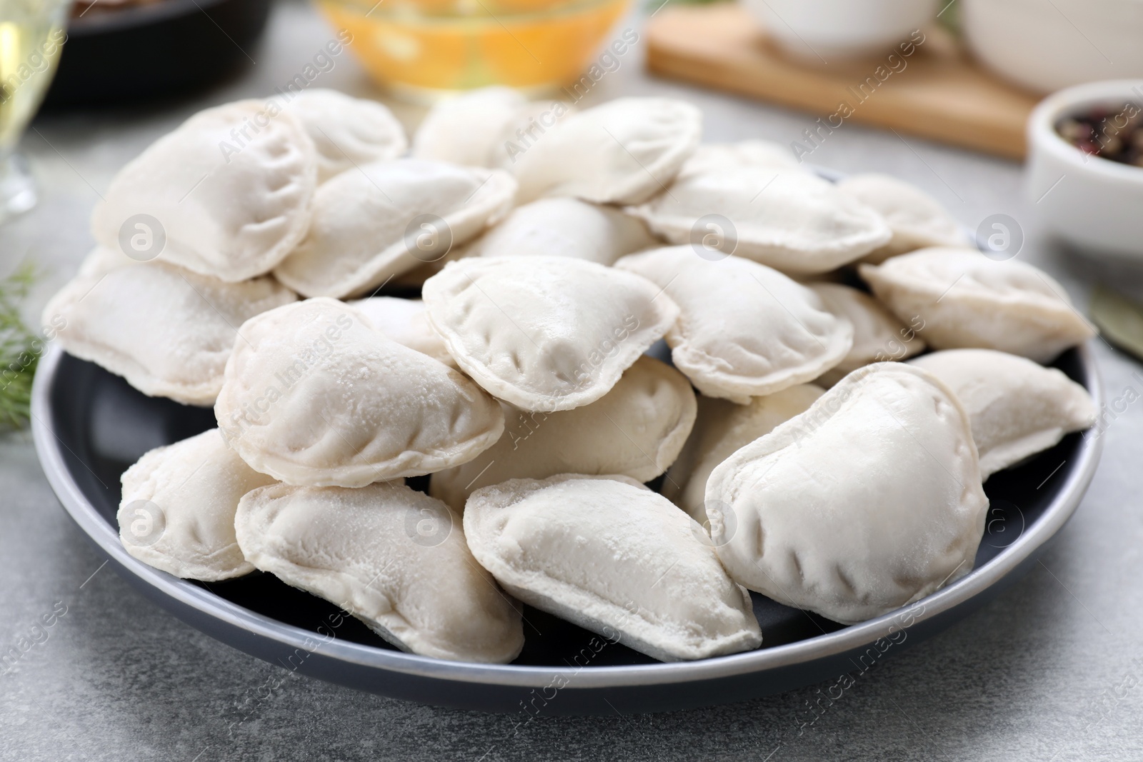 Photo of Raw dumplings (varenyky) and ingredients on grey table, closeup
