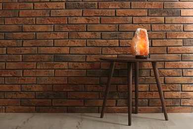 Himalayan salt lamp on table against  brick wall. Space for text