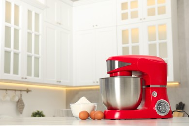 Photo of Modern red stand mixer, eggs and bowl with flour on white table in kitchen, space for text