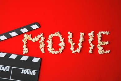 Clapperboard and word MOVIE made with popcorn on color background, top view. Cinema production