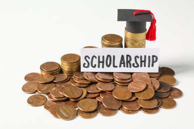 Photo of Paper with word Scholarship, graduation cap and coins on white table