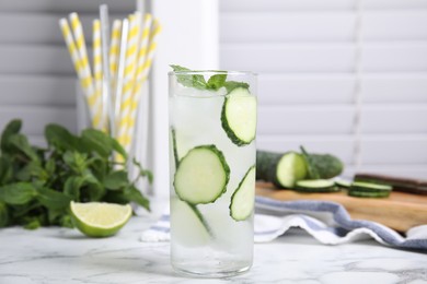 Glass of refreshing cucumber water with mint on white marble table