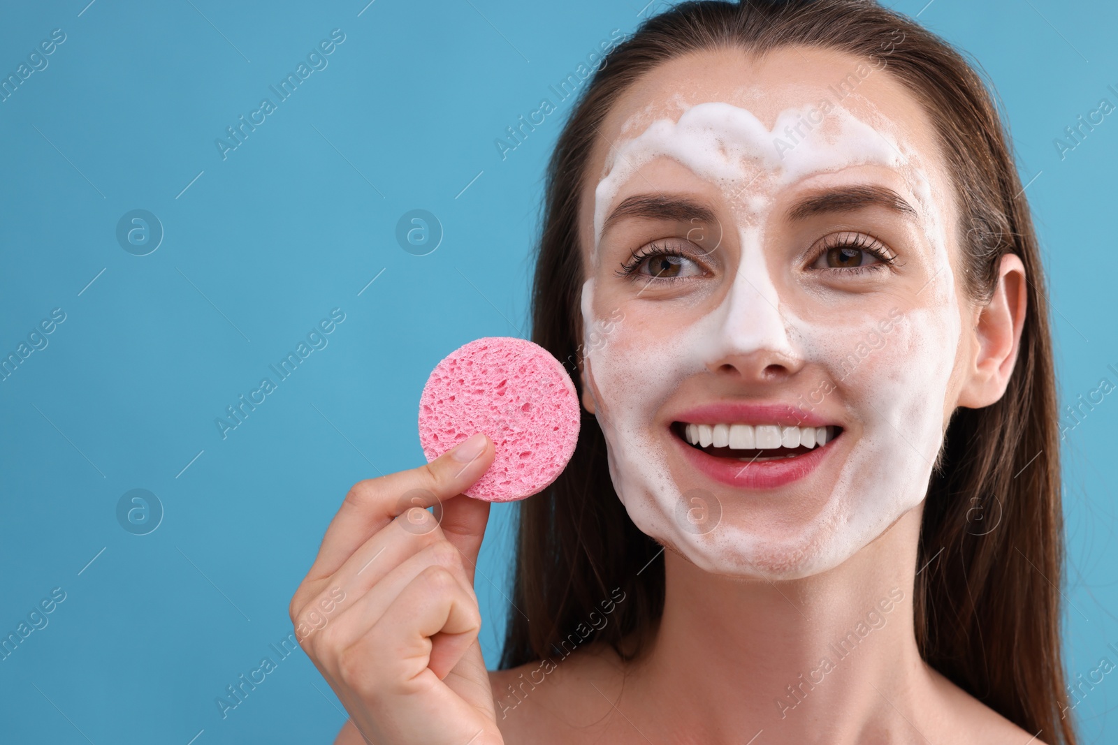 Photo of Happy young woman washing her face with sponge on light blue background. Space for text