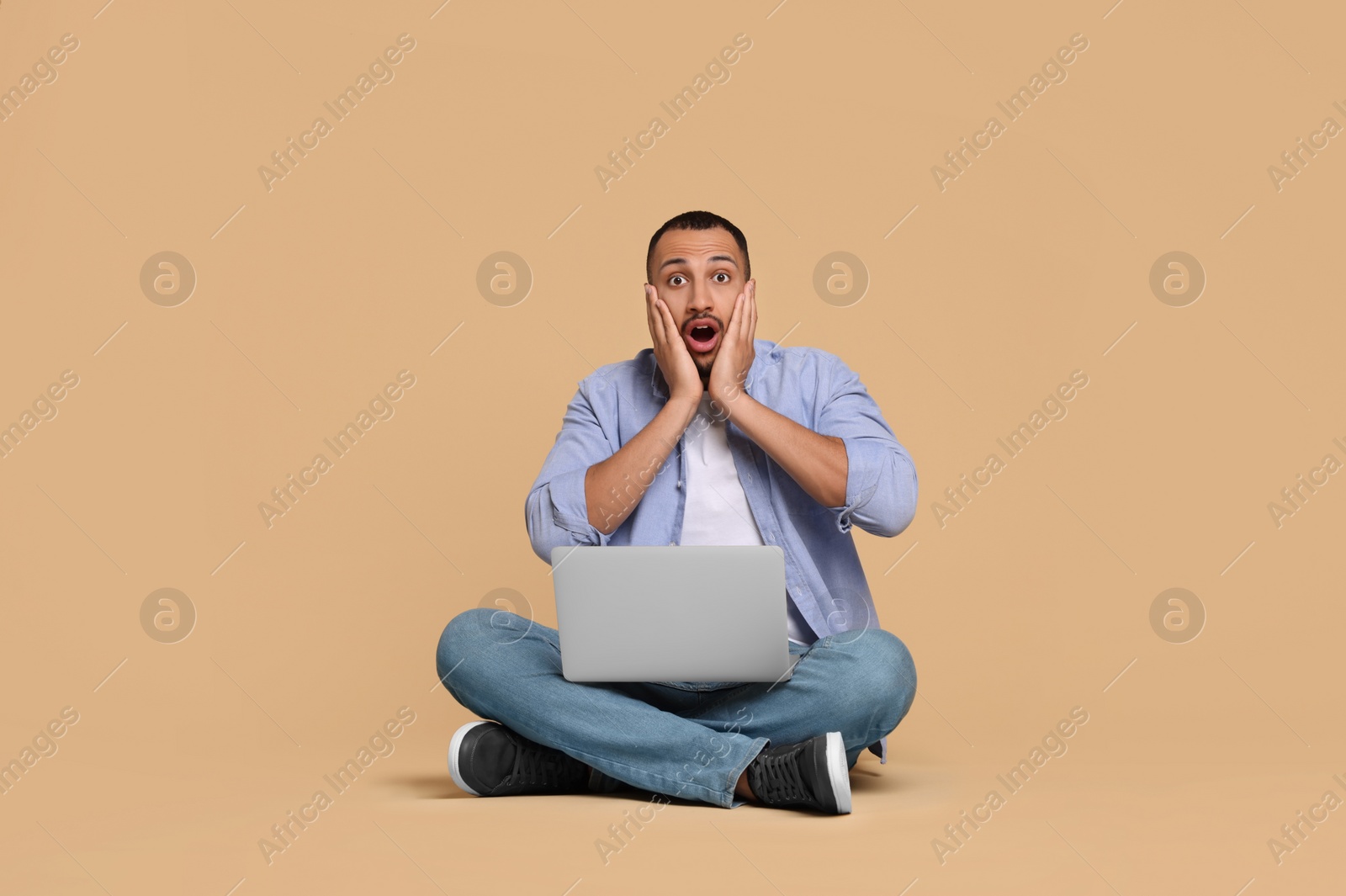 Photo of Surprised young man with laptop on beige background