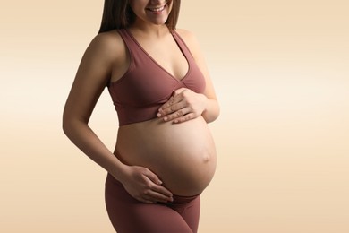 Image of Young pregnant woman touching her belly on beige background, closeup