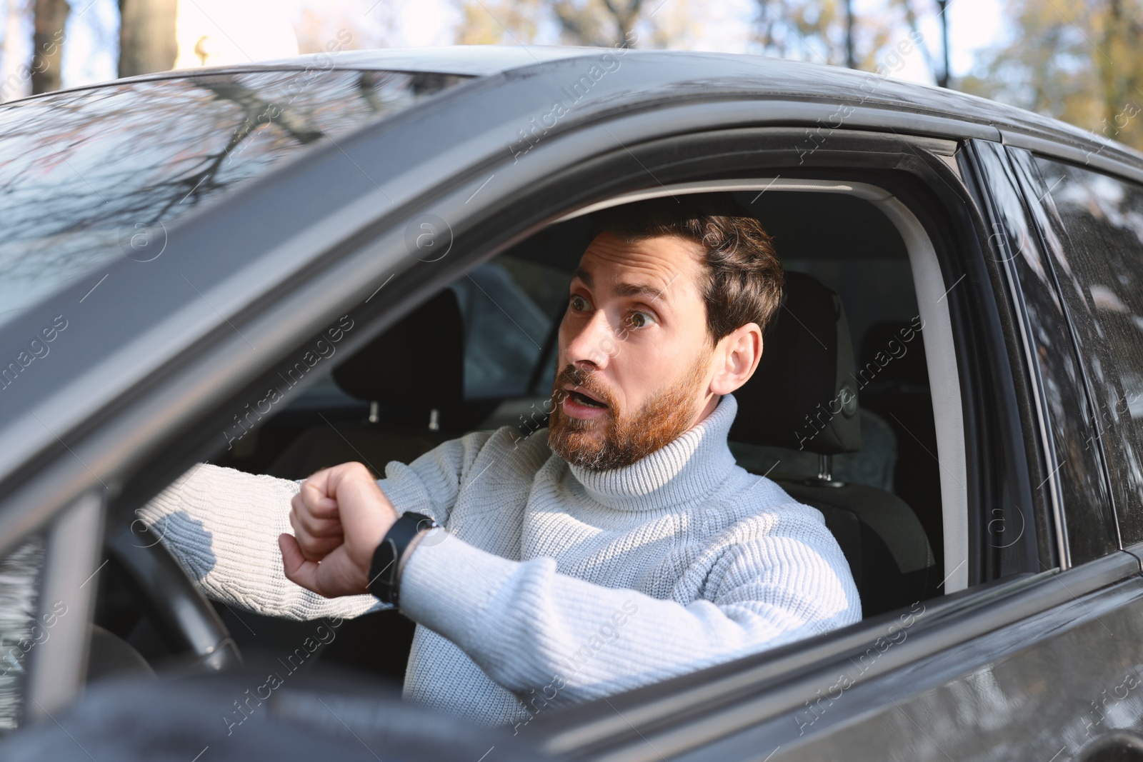 Photo of Emotional man checking time on watch in car. Being late concept