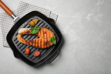 Frying pan with tasty salmon steak on grey background