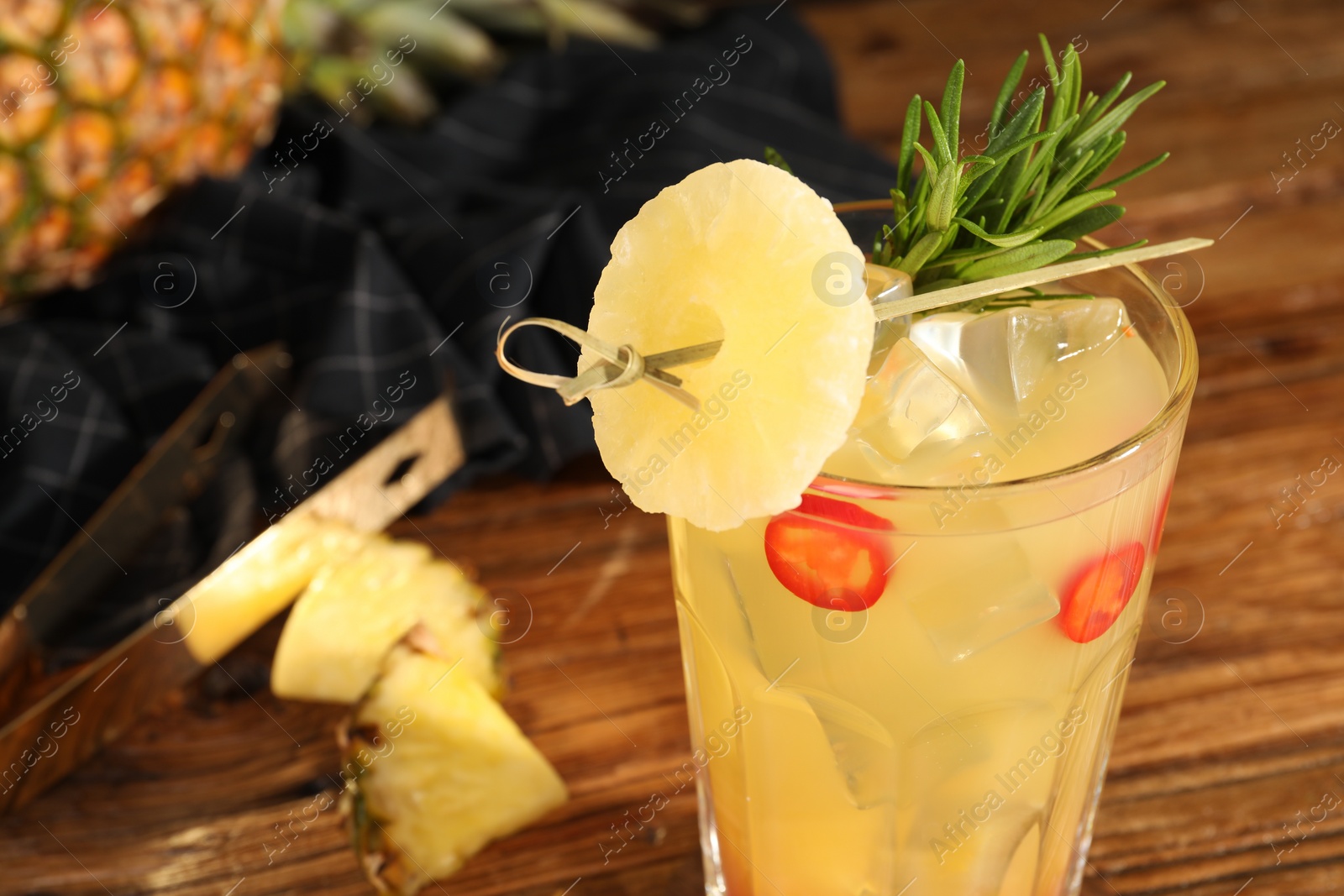 Photo of Spicy pineapple cocktail with chili pepper, rosemary and fresh fruit on wooden table, closeup. Space for text
