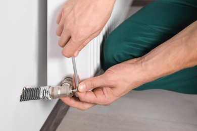 Professional plumber installing new heating radiator indoors, closeup