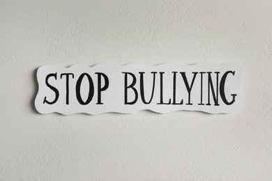 Photo of Paper card with text Stop Bullying on white stone surface, top view