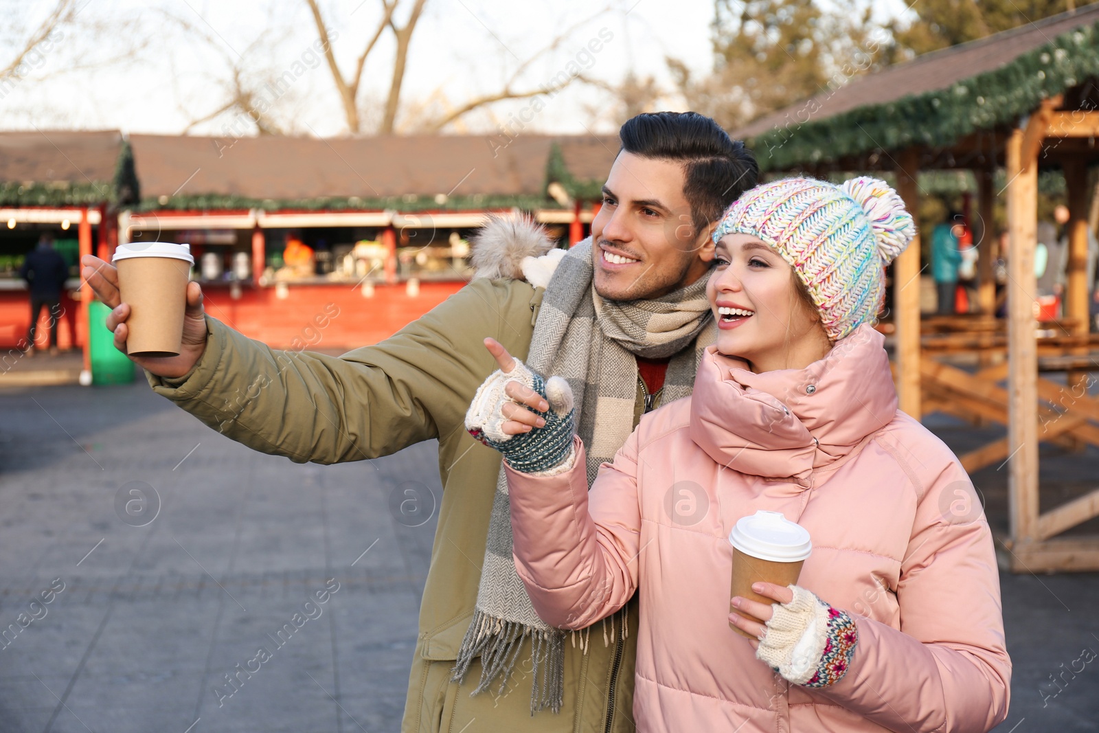 Photo of Happy couple in warm clothes with drinks at winter fair. Christmas season