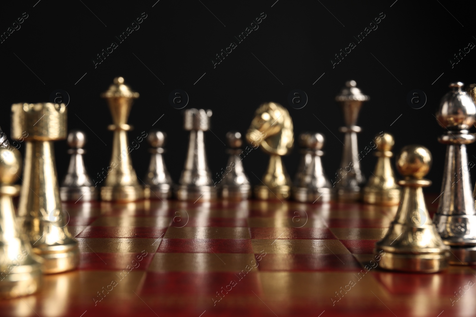 Photo of Many chess pieces on wooden checkerboard against black background, selective focus