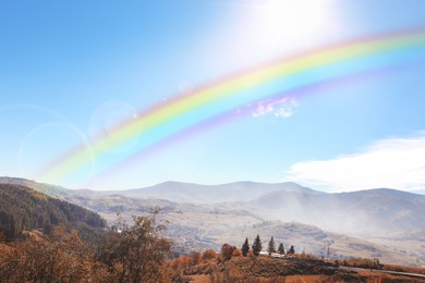 Image of Beautiful rainbow in blue sky over mountains on sunny day