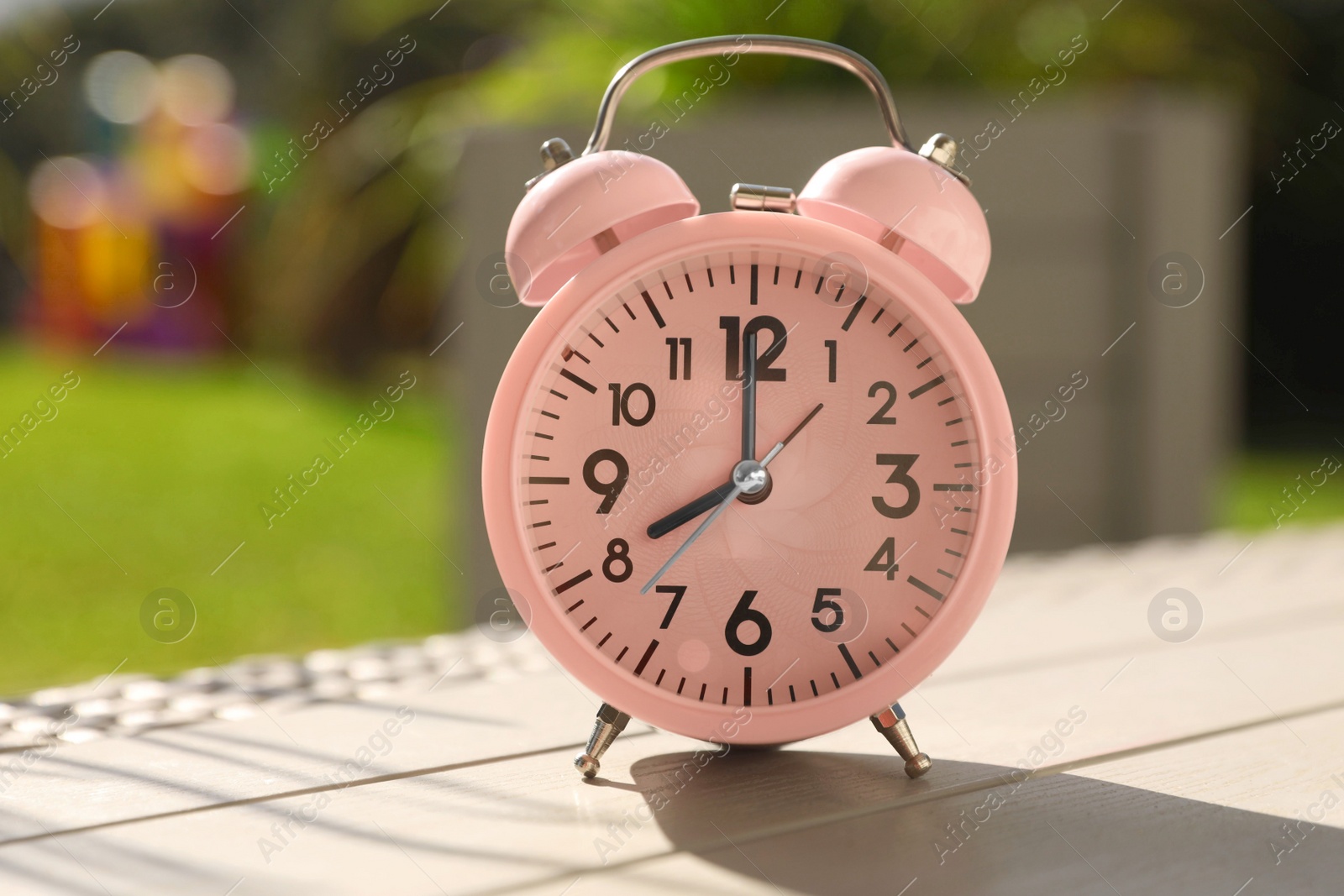 Photo of Pink alarm clock on table outdoors at sunny morning