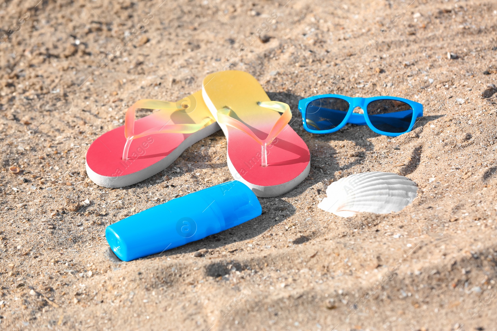 Photo of Sunglasses, bottle with sunscreen cream and flip flops on sand. Beach object