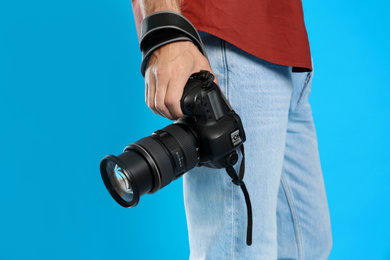 Professional photographer with modern camera on light blue background in studio, closeup