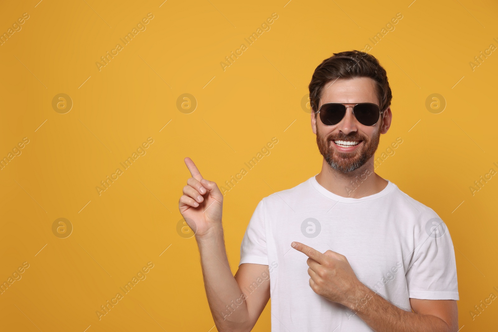 Photo of Portrait of smiling bearded man with stylish sunglasses on orange background. Space for text