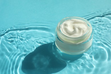 Photo of Jar with moisturizing cream in water on light blue background, closeup. Space for text