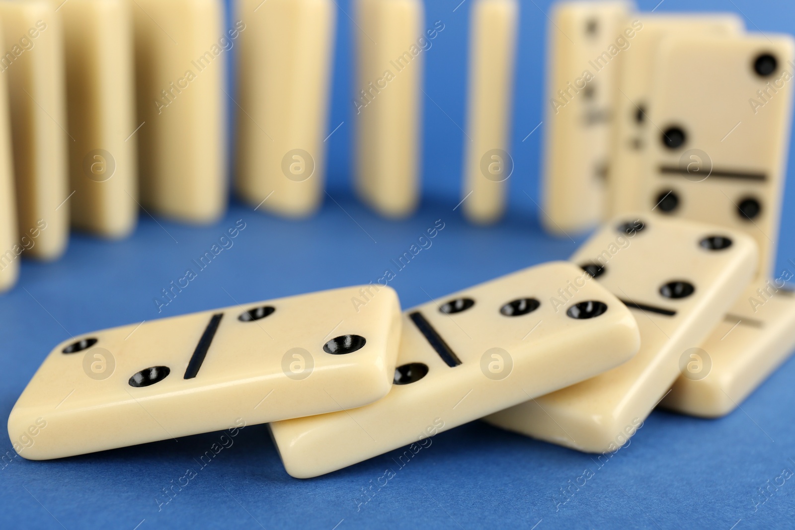 Photo of White domino tiles falling on blue background, closeup. Space for text