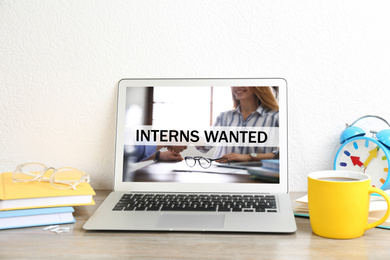 Image of Modern laptop with text INTERNS WANTED on wooden table