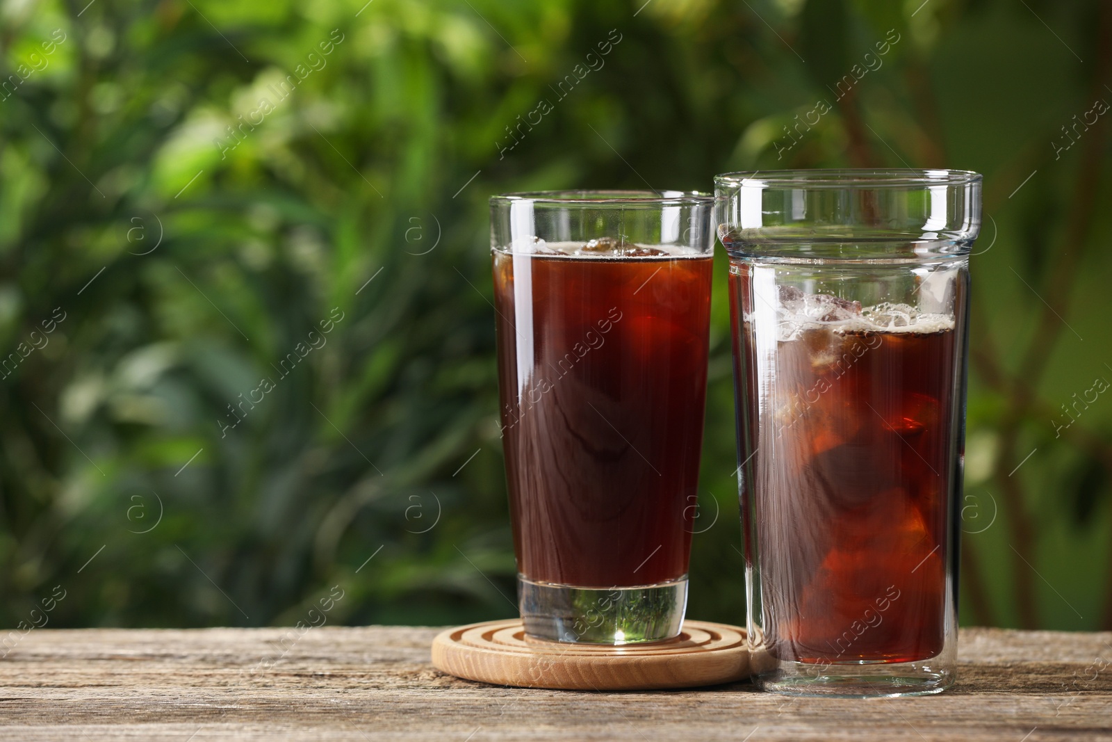 Photo of Glasses of fresh iced coffee on wooden table outdoors. Space for text