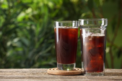 Photo of Glasses of fresh iced coffee on wooden table outdoors. Space for text