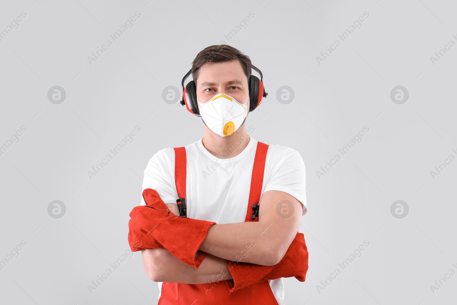 Photo of Male industrial worker in uniform on light background. Safety equipment